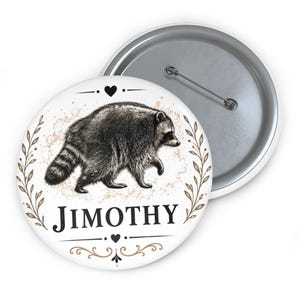 Op de afbeelding: Een ronde button met een gedetailleerde zwart-witillustratie van een lopende wasbeer. Het ontwerp bevat een bruine bladerkrans, kleine hartjes en de naam JIMOTHY gedrukt in een vetgedrukt zwart schreeflettertype op een witte achtergrond.