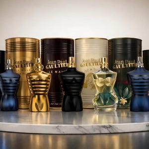 Könnte beinhalten: Eine Sammlung von Jean Paul Gaultier Düften, mit verschiedenen Flaschendesigns und Verpackungen. Die Flaschen sind torsoförmig und in Gold, Schwarz und Blau erhältlich. Die Verpackung umfasst zylindrische Behälter mit dem Markennamen.