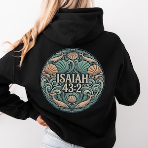 Könnte beinhalten: Ein schwarzer Kapuzenpullover mit einer kreisförmigen Grafik auf der Rückseite. Das Design zeigt stilisierte Wellen, Muscheln und Delfine in Blaugrün- und Beigetönen, mit dem Text "ISAIAH 43:2" in der Mitte in einer fetten Serifenschrift.