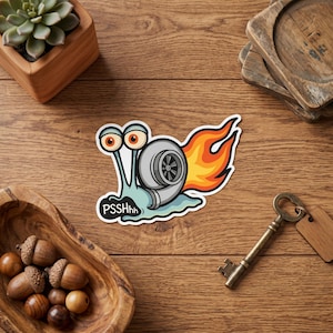 May include: A sticker featuring a cartoon snail with a turbocharger and flames. The snail is light blue with large orange eyes and the text "PSSSHhh". The turbo is silver and black, and the flames are orange and yellow.