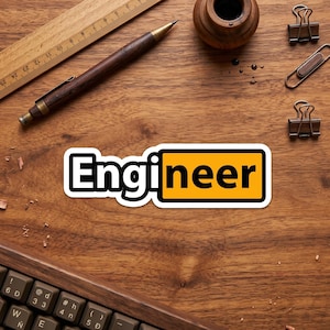 May include: A sticker with the word "Engineer" in a bold, black font with a yellow background. The sticker is on a wooden surface with a ruler, pen, inkwell, paper clips, and a keyboard.