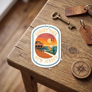 May include: A sticker featuring an illustration of Asbury Park, New Jersey, with a sunset over the ocean. The sticker includes the text "Asbury Park" and "New Jersey". A key, keychains, and a compass are also visible.