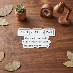 May include: A wooden desk with a succulent in a small wooden pot, a wooden clock, and a small wooden desk lamp. A sticker with the words "Ctrl + Alt + Del" and the phrases "Control yourself," "Alter your thoughts," and "Delete negativity" is on the desk.
