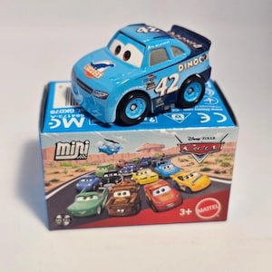 Könnte beinhalten: Ein hellblaues Spielzeugauto mit der Nummer 42 an der Seite, das auf einer Schachtel mit Rennwagen-Motiv steht. Das Auto hat schwarze Räder und das Wort "DINCO" an der Seite. Die Schachtel zeigt verschiedene Cartoon-Rennwagen.
