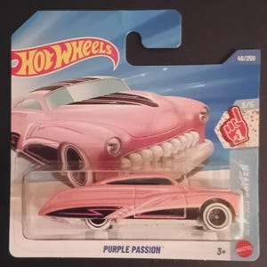 以下が含まれることがあります： 青と白のカードに、"Purple Passion"という名前のピンク色のホットウィールダイキャストカー。車は白と黒のアクセントと白いホイールが特徴です。カードにはホットウィールロゴと「#1」のフォームフィンガーグラフィックが含まれています。