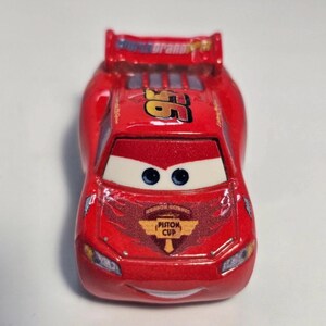 Może przedstawiać: Czerwony samochodzik z numerem 95 w kolorze złotym oraz napisami "Rust-eze" i "Piston Cup". Samoch&oacute;d ma niebieskie oczy i spojler. Zabawkowy samoch&oacute;d to replika Zygzaka McQueena z filmu Auta.