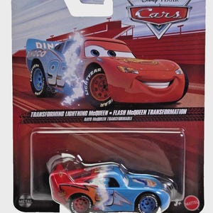 May include: A packaged Disney Pixar Cars toy featuring Lightning McQueen in a transforming design. The packaging shows the car in both red and blue color schemes, with the text "TRANSFORMING LIGHTNING MCQUEEN - FLASH MCQUEEN TRANSFORMATION". The toy is suitable for ages 3+.