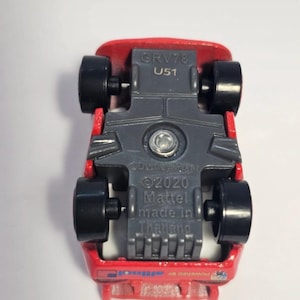 Może przedstawiać: Czerwony odlewany samoch&oacute;d zabawkowy z czarnymi kołami, widok od spodu. Samoch&oacute;d ma szare podwozie z napisem "GRV78 U51", "&copy;Disney/Pixar &copy;2020 Mattel made in Thailand" i "powered by allinol".