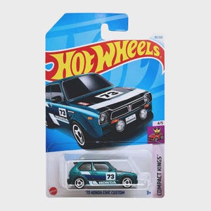以下が含まれることがあります： 青緑と黒の'73 Honda Civic Custom Hot Wheelsのダイキャストカー。青と白のカードにパッケージされています。車にはボンネットと側面に73の数字があります。カードにはHot Wheelsのロゴと「Compact Kings」の文字があります。