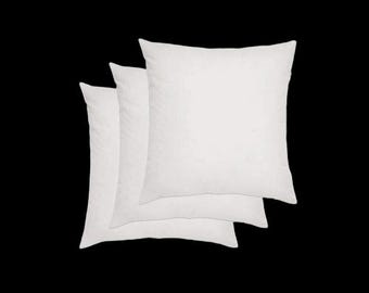 May include: Three square, white pillows are stacked on a black background. The pillows have a soft, fluffy appearance, suggesting they are filled with down or a similar material. The pillows are arranged in a slightly overlapping manner.