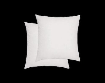 May include: Two square, white pillows against a black background. The pillows are fluffy and appear to be made of a soft material. The pillows are slightly overlapping, with one in front of the other.