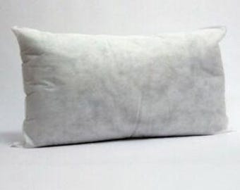 May include: A rectangular white pillow, likely for decorative use, is shown against a white background. The pillow has a soft, slightly textured appearance, suggesting a comfortable filling. The pillow is approximately 18 inches long.