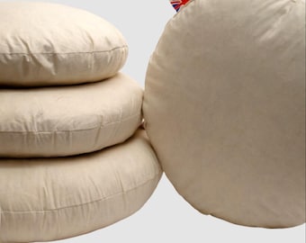 May include: A stack of four round, beige cushions. The cushions are made of a textured fabric and have a stitched seam around the edge. One cushion has a tag with a Union Jack flag.