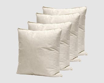 May include: Four off-white square pillows arranged diagonally. The pillows have a soft, textured appearance and are likely made of a natural fabric. The neutral color and simple design suggest a minimalist or farmhouse style.