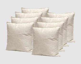 May include: A collection of nine off-white square pillows arranged in a layered display. The pillows have a soft, slightly textured appearance, suggesting a comfortable, inviting quality. The neutral color palette makes them versatile for various home decor styles.