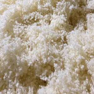May include: Close-up of a pile of fluffy, off-white material. The texture appears soft and cloud-like, with a dense, irregular structure. The material is likely a natural fibre, possibly wool or cotton, used for stuffing or padding.