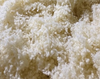 May include: Close-up of a pile of fluffy, off-white material. The texture appears soft and cloud-like, with a dense, irregular structure. The material is likely a natural fiber, possibly wool or cotton, used for stuffing or padding.