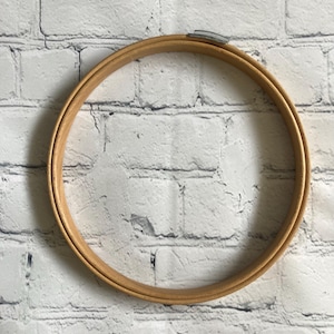 May include: A circular wooden embroidery hoop featuring a light brown natural wood finish and a silver-toned metal tension screw mechanism at the top, designed for holding fabric taut during needlework projects and craft applications.
