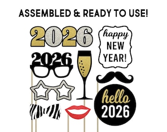 May include: A selection of New Year's Eve photo booth props on sticks. Features gold and silver glittered "2026" numbers, glasses, star-shaped glasses, a bow tie, lips, a champagne glass, a mustache, and a "hello 2026" sign. The words "ASSEMBLED & READY TO USE!" and "happy NEW YEAR!" are also visible.