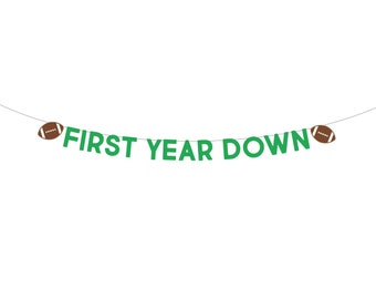 May include: Green and white banner with the text "FIRST YEAR DOWN" and brown footballs at each end.