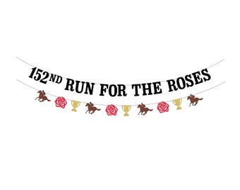 May include: A banner with the text "152ND RUN FOR THE ROSES" in black. The banner is decorated with brown horses, red roses, and gold trophies, all hanging from a string against a white background.