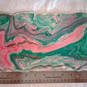 May include: A rectangular resin tray with a marbled design in shades of pink, green, and silver. The tray has black handles and measures approximately 12 inches long. The edges of the tray have a wavy design.