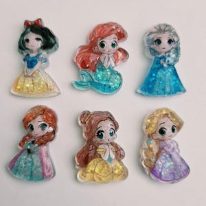 May include: Six colourful resin figurines of cartoon princesses. Each princess has a unique hairstyle and dress, with glitter accents. The princesses include Snow White, Ariel, Elsa, Anna, Belle, and Rapunzel. The figurines are on a white background.