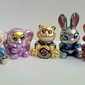 May include: A collection of five iridescent animal figurines: a dog, elephant, bear, rabbit, and fox. Each figurine is brightly colored with a pearlescent finish. The figures are sitting down, with large eyes and detailed features.