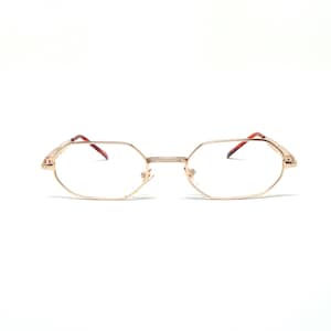 May include: Gold-tone eyeglasses with a geometric frame and clear lenses. The glasses have a thin bridge and temples with brown tips. The overall design is minimalist and classic, suitable for everyday wear.
