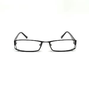 Peut inclure: Lunettes rectangulaires noires avec des verres transparents. Les montures sont noir mat, avec un pont et des branches fins. Les lunettes sont posées sur un fond blanc.