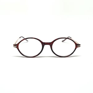 Könnte beinhalten: Runde Brille mit einem dunkelbraunen Schildpattrahmen und goldfarbenen Bügeln. Die Gläser sind klar, und die Brille ist vor einem weißen Hintergrund platziert. Das Gesamtdesign ist klassisch und stilvoll.