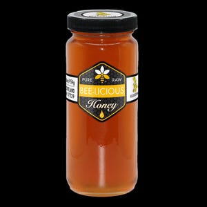 May include: A glass jar of honey with a black lid and a label that reads "Bee-licious Honey." The label features a bee graphic and the words "Pure Raw." The jar contains golden-colored honey and is set against a black background.