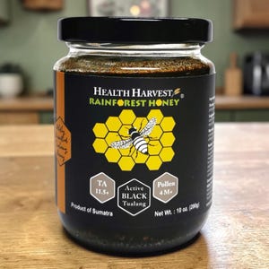 May include: A jar of Health Harvest Rainforest Honey with a black lid and label. The label features a honeycomb design with a bee illustration. Text on the label includes "TA 11.5+", "Active Black Tualang", and "Pollen 4M+". The net weight is 10 oz (280g).