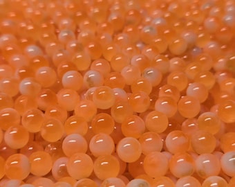 May include: A large collection of small, round, translucent orange beads. Each bead features a smooth, glossy surface with subtle variations in colour intensity, ranging from pale peach to vibrant tangerine, creating a uniform texture.