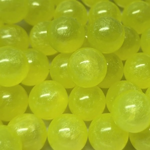 Könnte beinhalten: Eine Ansammlung zahlreicher kleiner, kugelförmiger Perlen in einer leuchtenden, durchscheinenden neongelben Farbe. Jede Perle hat eine glatte, polierte Oberfläche, die das Licht reflektiert und ein einheitliches, helles Erscheinungsbild erzeugt.