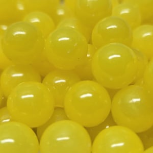 Könnte beinhalten: Eine Ansammlung zahlreicher kleiner, glatter und kugelförmiger gelber Perlen. Jede Perle hat eine glänzende, reflektierende Oberfläche, die das Licht einfängt und helle Glanzlichter auf der einheitlichen, leuchtend gelben Farbe der runden Objekte erzeugt.