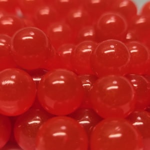 Könnte beinhalten: Eine Ansammlung kleiner, runder, durchscheinender roter Perlen mit einer glatten, glänzenden Oberfläche. Die Perlen sind dicht beieinander angeordnet und bilden einen Haufen aus leuchtenden, gleichmäßigen Kugeln, die das Licht auf ihren polierten Oberflächen reflektieren.