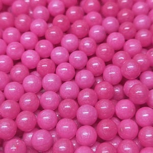 May include: A close-up of many small, round, shiny, hot pink spheres. The spheres are tightly packed, creating a textured surface with highlights and shadows. The image is dominated by the vibrant pink colour.