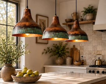 May include: Three bell-shaped pendant lights hanging from black cords. Each fixture features a weathered copper finish on the upper section and a textured, oxidised teal green patina along the lower rim, with a warm metallic interior glow.