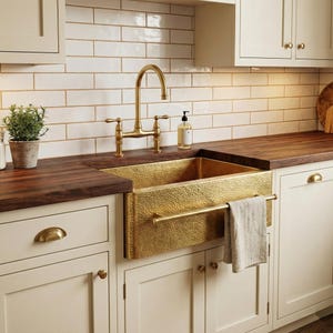 May include: A gold hammered-finish kitchen sink and tap. The sink is set into a dark wood countertop, with cream-coloured cabinets below. A small potted plant and soap dispenser are also visible.