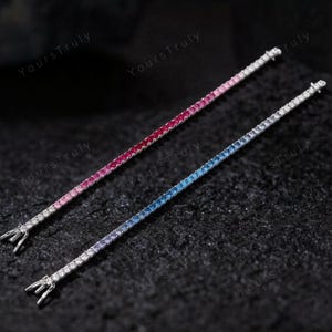 May include: Two delicate tennis bracelets. One features a gradient of pink to red gemstones, the other a gradient of blue to purple gemstones. Both bracelets have a silver clasp and are set against a dark, textured background.
