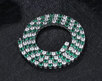 May include: A silver-toned tennis necklace with alternating emerald green and clear cubic zirconia stones. The necklace is displayed on a dark, textured surface. The brand name "YoursTruly" is visible in the background.