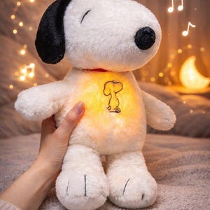 May include: A plush Snoopy toy with a black ear, black nose, and a red collar. The toy has a glowing belly with a Snoopy outline. Musical notes and a crescent moon light up the background.
