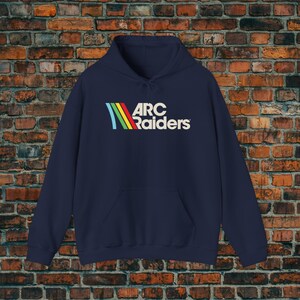 May include: Navy blue hooded sweatshirt with a front pocket and drawstring. The sweatshirt features the text "ARC Raiders" in white, with a colorful, stylized graphic above the text.