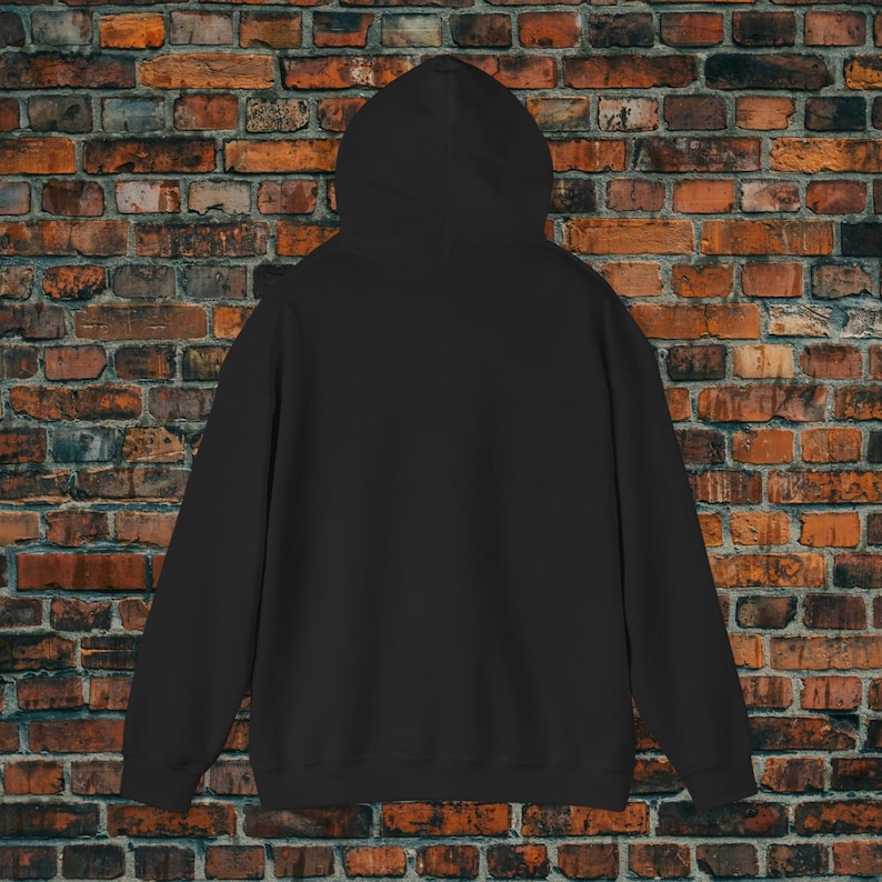 May include: A solid black hoodie with a hood, long sleeves, and a kangaroo pocket. The hoodie is made of a soft material and is displayed against a brick wall background.