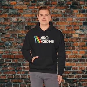 May include: Black hooded sweatshirt with the text "ARC Raiders" in white, with a colorful logo above the text. The logo features a blue, yellow, and red design. The sweatshirt has a front pocket and a drawstring hood.