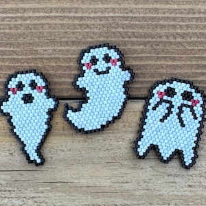 May include: Three white beaded ghost ornaments with black outlines and pink cheeks. The ghosts have different facial expressions.