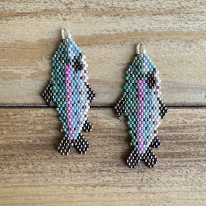 May include: A pair of beaded fish earrings with a pink, blue and green colour scheme. The fish are detailed with black beads for the eyes and fins.