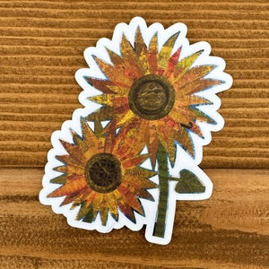 May include: Two sunflowers with a vintage newspaper collage design. The sunflowers are yellow, orange, and brown with a green stem and leaf.