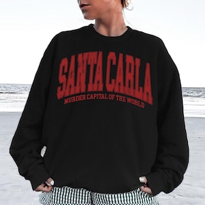 May include: A white ceramic mug with a black handle and the text "But First, Coffee" in a bold, black font. The mug is set against a blurred background, suggesting a cozy setting.